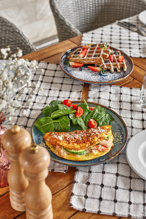 Bio heathy food - fresh omelet with salad and waffle with strawberry and cream. Served table at...