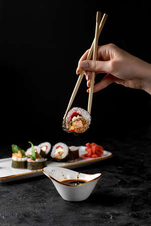 Hand holding Futo maki with chopstick on dark background.の写真素材