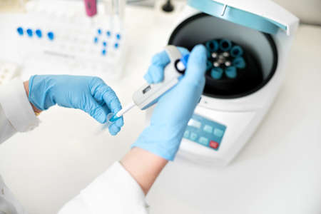 researcher using pipette and analysis flask samples into a centrifuge in laboratory.