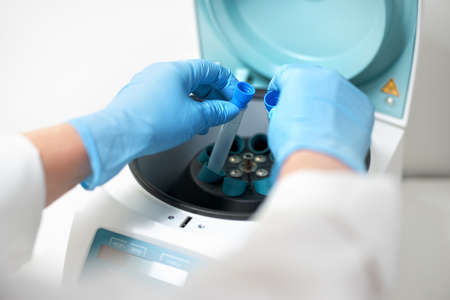 Females hand in blue glove putting analysis samples into a centrifuge in laboratory.の写真素材