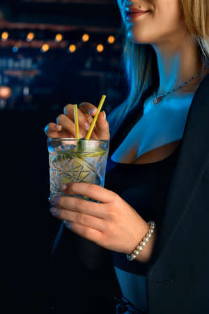 Young woman in a bar or club having fun - in the background her bar, focus on the glass mojito she is holding in her handの写真素材