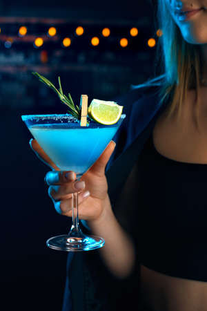 Young woman in a bar or club having fun - in the background her bar, focus on the glass she is holding in her handの写真素材