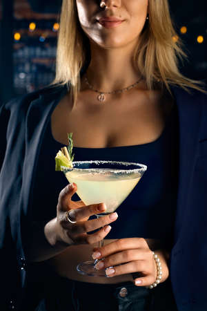 Young woman in a bar or club having fun - in the background her bar, focus on the glass she is holding in her handの写真素材