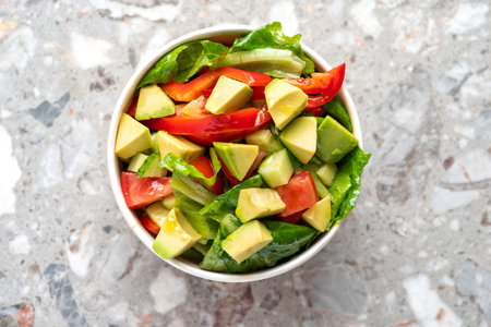 Avocado and fresh tomatoes salad in bowl on gray stone background top view. Concept Food For Parties. fast food. Healthy lunch. Food delivery in disposable plate of craft paper. Eco-friendly cardboard packaging environment protectionの写真素材