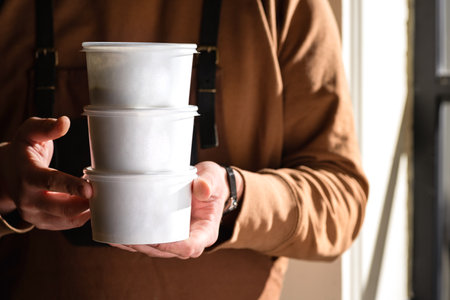 Stack of food delivery boxes. Anonymous hands holding stack of delivery boxes. Craft packaging of delivered food in hands. Mockup for delivery of fast foodの写真素材