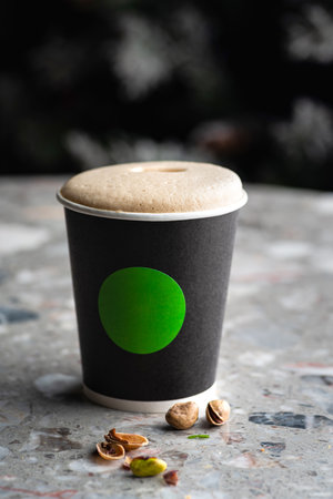 Cappuccino in a paper glass on a marble table, with the taste of pistachio, an addition to coffee. Coffee cup mockup for branding.の写真素材