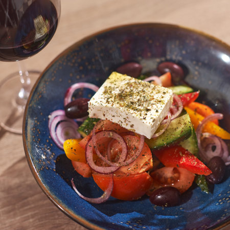 Classic Greek salad of tomatoes, cucumbers and cheese. Plate of salad and a glass of wine on a table.の写真素材
