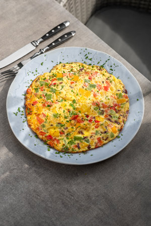 Filled omelette with tomatoes, red bell pepper and broccoli on light wooden table. Healthy diet food...