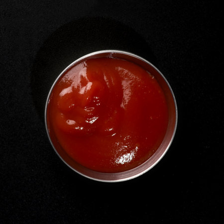Ketchup in a metal gravy boat on a black background dope for fast food, top viewの写真素材