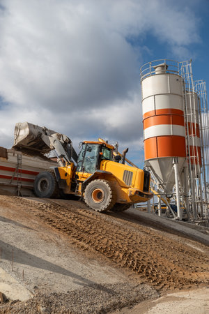 The front loader unloads the crushed stone into the making machine concrete. Against the background of the production room. heavy equipment.の写真素材