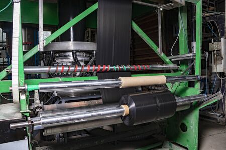 Production of garbage bags rolls. The extruder blows out a sleeve of black plastic film from recycled waste pellets. Black plastic garbage bags roll up. Recycling plant.の写真素材