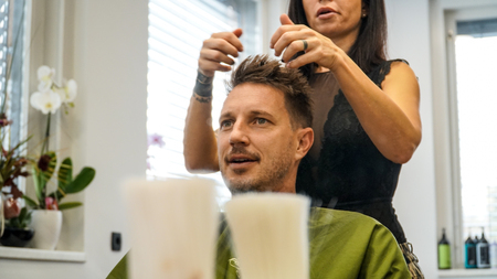 A man getting his hair cut by a woman hairdresser with tatoos