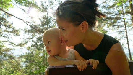 A cute baby boy with his beautiful mother in nature. Sun flair