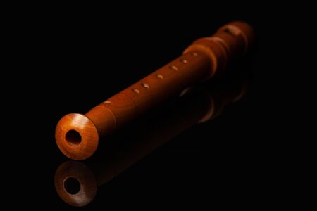 A wooden flute lies on a black glossy glass in which its reflection is visibleの写真素材