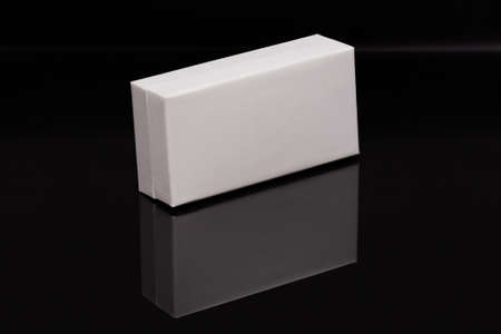 A white oblong gift box stands on a black glass, in which its reflection is visibleの写真素材