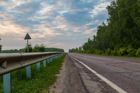 Country road on the edge of the forest against the evening sky