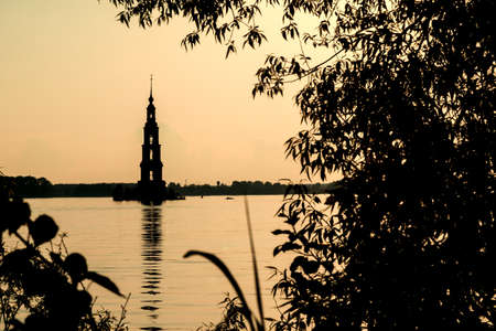 Silhouette of a flooded bell tower in the city of Kalyazin and coastal trees against the evening sky, Russiaの写真素材