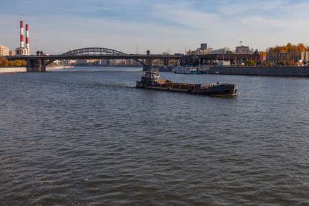 A barge is floating on the river against the background of an automobile bridge and factory pipes.の写真素材