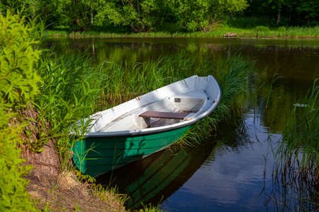 Old green fishing boat stands in the grass near the river bank.の写真素材