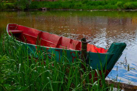 An old many times repainted fishing boat stands next to the shore, tied to a chainの写真素材