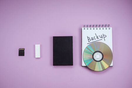 history of data storage devices on a lilac background. dvd, flash drive, hard drive, sd card top view. Notepad backup textの写真素材