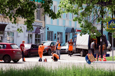 Team of road workers in orange uniforms make a pedestrian crossing in the city. Specialists applied the paint to the roadway. Kolomna, Moscow region/Russia - 06.06.2020.のeditorial素材