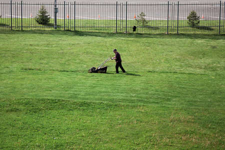 gardener mows the lawn in the city. Work of municipal services in the summer. Kolomna, Moscow region/Russia - 06.06.2020.のeditorial素材