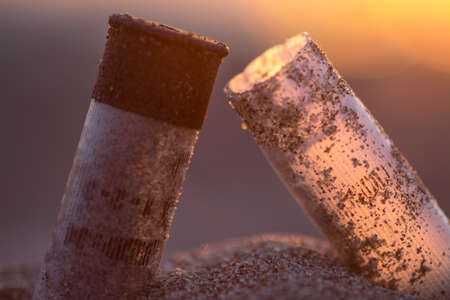 Cigarette stubs in the sand on a sunset background.