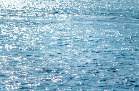 Blue water background. Water surface texture. Blue water surface with sun reflectionsの写真素材