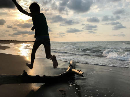 Silhouette of a boy jumping on the beach at sunset.の写真素材