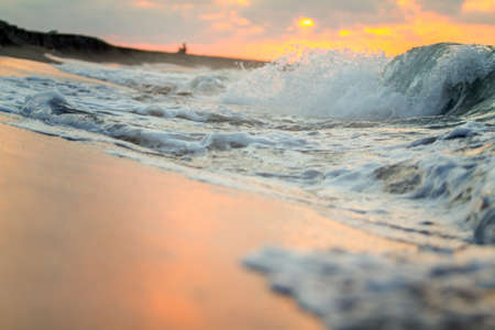 Beautiful sunset on the beach with waves and foam on the sand.