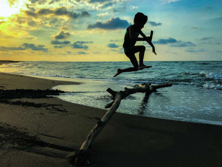 silhouette of a boy jumping on the beach at sunset.の写真素材
