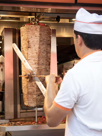A man in a white T-shirt and a blue hat is preparing kebab in a restaurantの写真素材