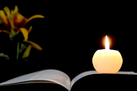 Candle, opened book and flowers isolated on black backgroundの写真素材