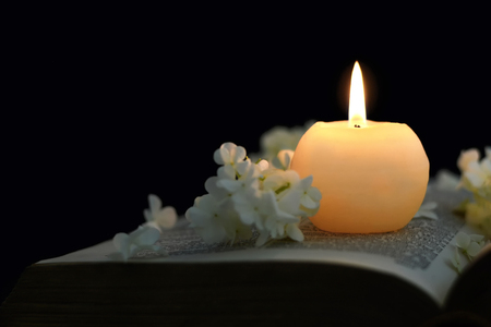 Burning candle and white flowers on opened book