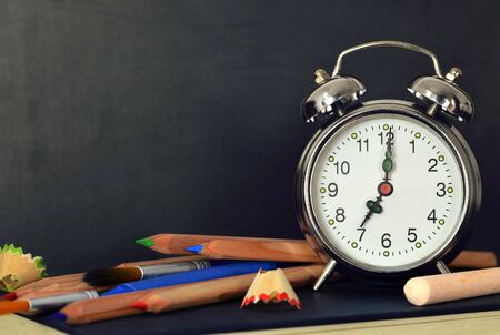 Back to school. School supplies and alarm clock with blank blackboard in backgroundの写真素材