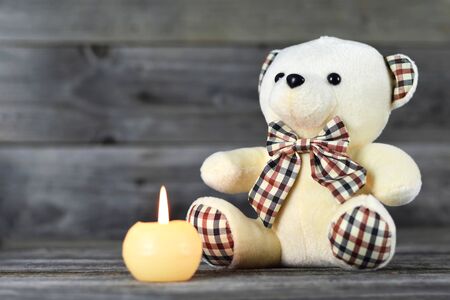 Teddy bear and white candle on wooden backgroundの写真素材