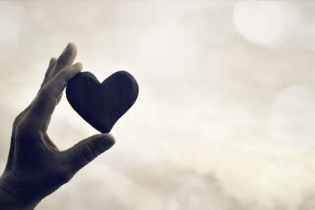 Black and white image of hand holding a heart against skyの写真素材