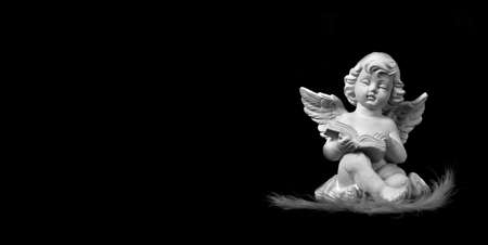 Angel sitting and reading book isolated on black backgroundの写真素材
