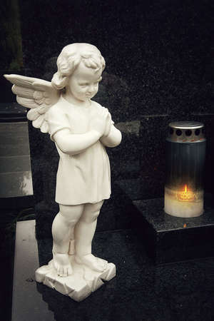Guardian angel figurine and burning candle on the graveの写真素材
