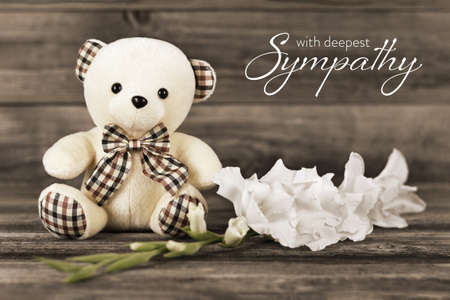 Sympathy card with teddy bear and white flower on wooden background