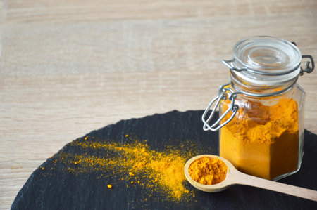 Turmeric powder in the wooden spoon on black slate, close upの写真素材