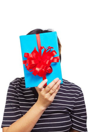 Asian female hide her face behind gift  box wrapped in bright blue color box with red ribbon and bow. The most beautiful gift isolated on white backgroundの写真素材