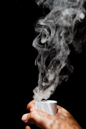Electronic Cigarette or vaper is activating and release a cloud in a human hand, black color backgroundの写真素材