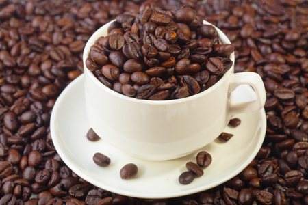 Coffee beans in a white cup on a pile of coffee bean backgroundの写真素材