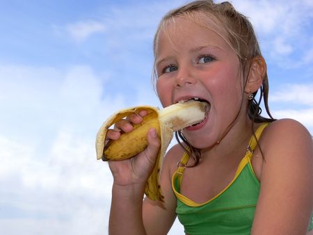 Little girl eating a banana on the beachの写真素材