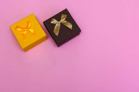 Two Christmas bright gift box with ribbon tied with a bow on a pink background with a place for inscription.の写真素材