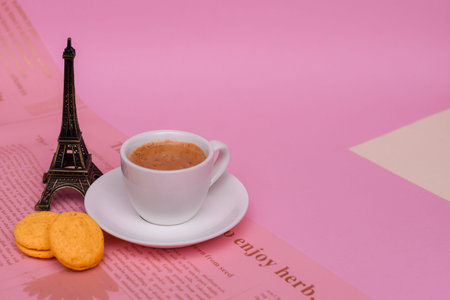 Cup of coffee and colorful macaron or macaroon next to Eiffel Tower on pink background.