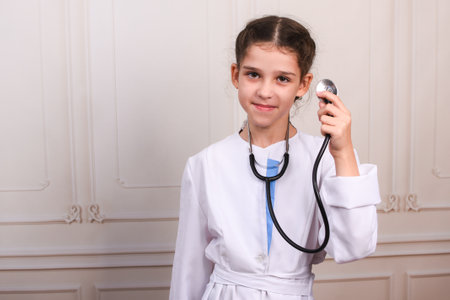 Cute child in doctor coat with stethoscope on light background. Girl plays doctor. Space for text.の写真素材