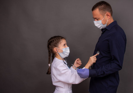 Child girl in doctor coat with stethoscope plays doctor. Adorable kid in medical lab coat pressing...